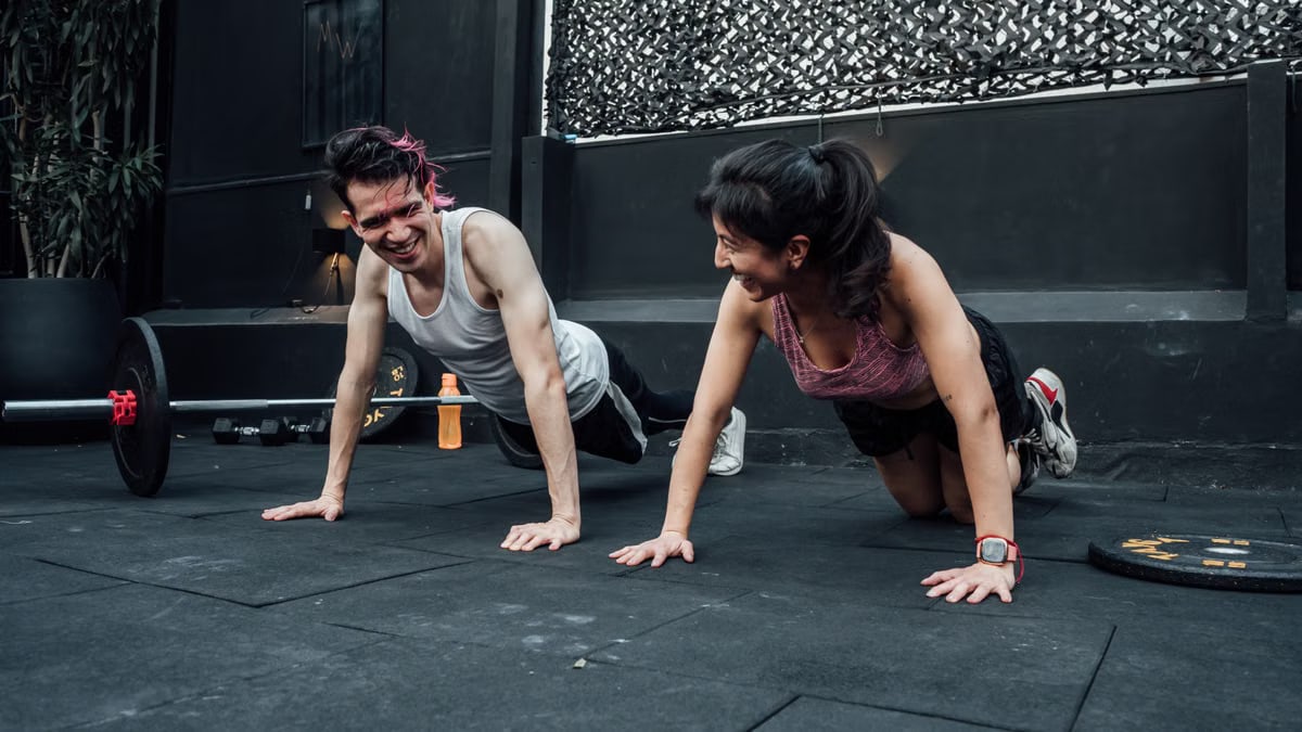Man and woman doing pushups while smiling during a workout inside a Mexico City gym.