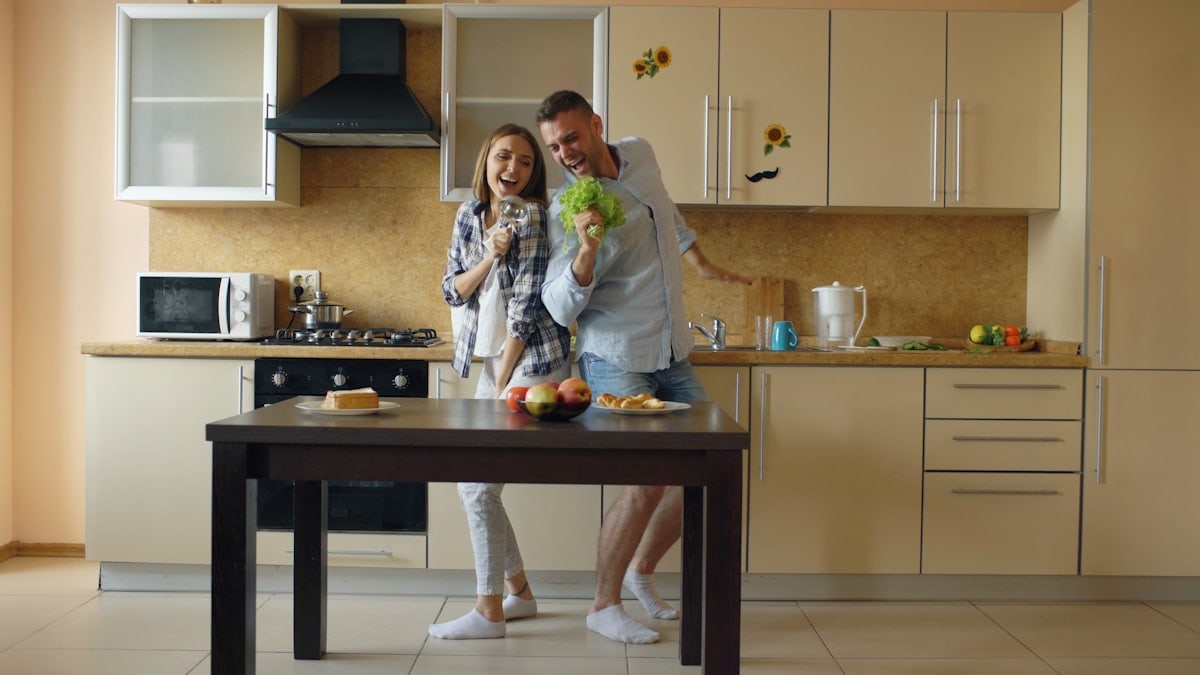 Attractive young joyful couple have fun dancing and singing while cooking in the kitchen at home in the morining
